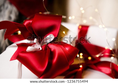 Lovely presents under Christmas tree, gift boxes on white, fluffy, cozy blanket background with glowing reindeer decoration and fairy lights. Concept of holidays, giving gifts, love and surprises. 
