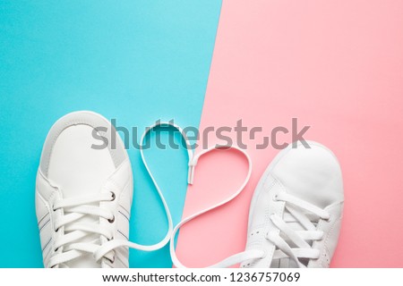 Heart created from white shoelaces between male and female sport shoes. Love concept. Top view. Empty place for lovely, cute text, quote or sayings on pastel blue and pink paper background. Closeup.