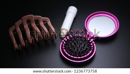 Mirror comb, hair clip, hygienic lipstick on a black background
