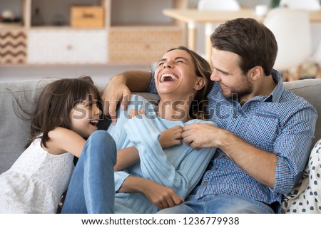 Cheerful people sitting on couch in living room have fun little daughter tickling mother laughing together with parents enjoy free time playing at home. Weekend activity happy family lifestyle concept Royalty-Free Stock Photo #1236779938