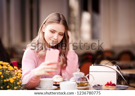 Smiling teenage girl 14-16 year old making selfy in cafe outdoors. Looking at phone camera. 