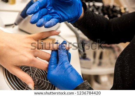 Offering color. Experienced nail artist wearing white shirt and bright gloves offering nice nail polish colors her client
