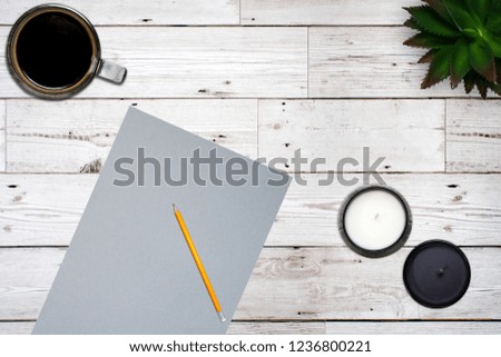 A desk layout featuring grey card, pencil, coffee, candles and a succulent plant on a vintage wood background