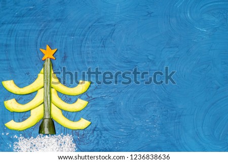 Bright flat food concept of celebrating Christmas and New Year. Christmas tree made from avocado, cucumber and carrots, snow drift from sea salt. Top view Copy space