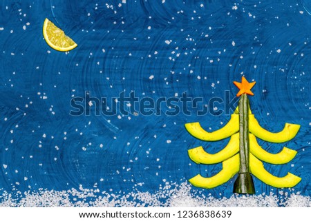 Bright flat food concept of celebrating Christmas and New Year. Christmas tree made from avocado, cucumber and carrots, moon made from lemon wedge, snow from sea salt. Top view Copy space