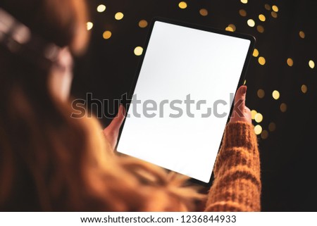 Woman using tablet computer at night with dramatic lighting and shallow depth of field. Blank screen with bright lighting for design mockups.