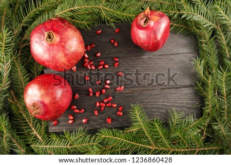 Still-life with pomegranates and fir branches on the background of a black wooden board