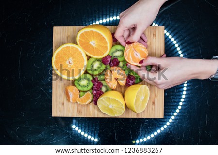 Close up picture of a mix of  diferent spring  fruits in a dark background. orange, kiwi, berries, wooden plate