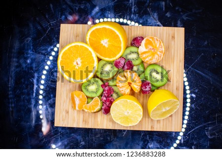 Close up picture of a mix of  diferent spring  fruits in a dark background. orange, kiwi, berries, wooden plate