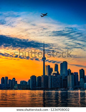 TORONTO CITY SKYLINE AT SUNSET - Beautiful sunset scene of Toronto cityscape in summer with airplane flying past dramatic sky. Blue and orange colors. International travel abroad. Toronto, Canada
