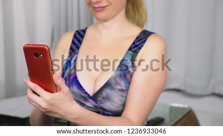 Beautiful girl use a cellular smartphone while sitting in the living room in the evening. Happy smiling young woman chatting on the internet at home.