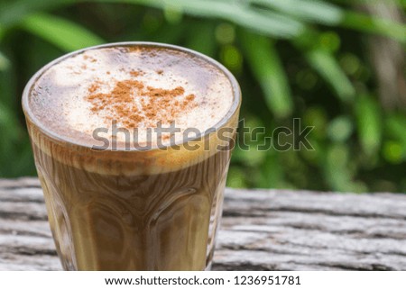 Latte Coffee in Glass on Wood Table with Natural Green Tree Background Zoom. Latte coffee in coffee shop or cafe
 with nature green tree 
relax emotion background