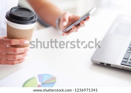 Woman using a smartphone and holding a cup of coffee in her office.