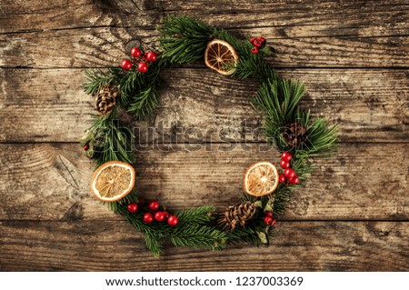 Christmas wreath of Fir branches, cones, red decoration on wooden background with snowflakes. Xmas and Happy New Year theme. Flat lay, top view
