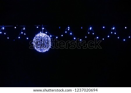 city street christmas decoration. blue lights garlands and glowing decorative ball against night sky background