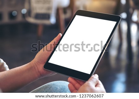 Mockup image of hands holding black tablet pc with blank white screen while sitting in cafe