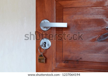 Open dark brown wooden door with key  in keyhole with house shaped pendant with copy space for text on light wall. Real estate rent house or buy new home concept.
