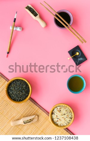 Chinese traditional symbols concept. Tea, rice, hieroglyph symbol, bambootabe mat, chopsticks, soy sause on pink background top view frame copy space
