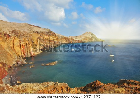 Madeira. Picturesque white yachts in the rocky gulf in the east of the island. Shining rays of the sun reflected in the water
