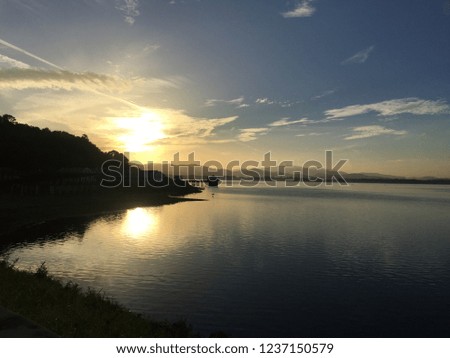 Sunrise at the reservoir on left hand side of picture. Blue sky is background. The sun reflects on the surface. The mountain is in the lower left corner.