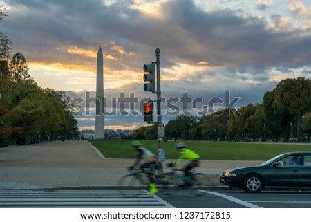 Horizontal View of the Obelisk in Washington DC at Sunset with two Bikers Running in the Street on Cloudy Sky Background