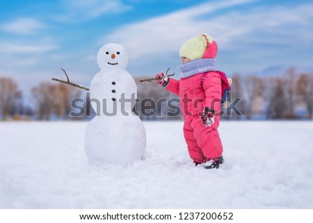 Cute child girl making snowman at bright snowy place. Winter outdoor activities