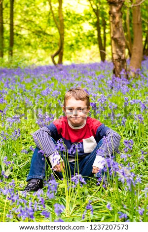 A handsome little boy with ADHD, Autism, Aspergers Syndrome sits and poses for a picture in a forest, woods covered in Bluebells, (Hyacinthoides non-scripta)