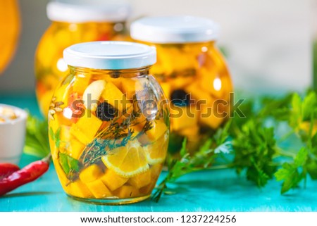 Marinated preserving jars. Homemade orange cut pumpkin pickles with red hot chili peppers, fresh parsley, spices on light turquoise wooden background. Fermented food.