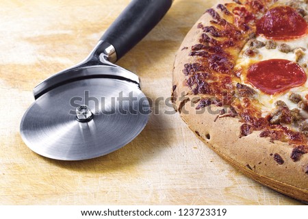 Image of pizza slicer and pepperoni pizza in wooden table