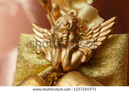 close-up of golden cherub figure with two jingle bells. Elegant christmas decoration with Smiling cherub copper colored and two jingle bells on brown background. Cherub for Christmas tree on canvas