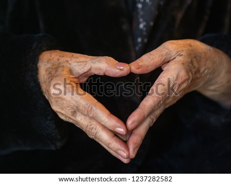 Close-up of hands senior woman showing heart figure with fingers. Love concept