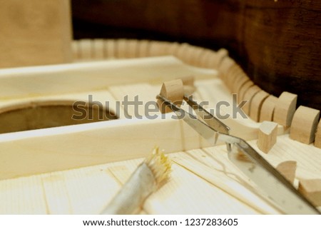 Luthier gluing parts harmonica structure top with brush and tweezers of a classical guitar