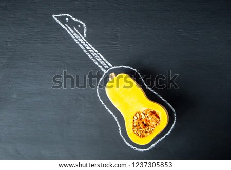 Halve of raw organic pumpkin in form of guitar and a picture of guitar on a black slate, stone or concrete background.Top view
