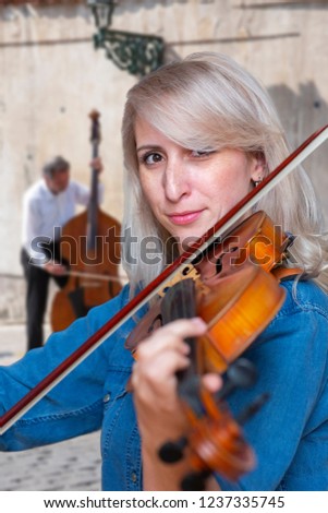 A beautiful blonde girl in black dress with red lips plays a violin closeup Limited depth of field