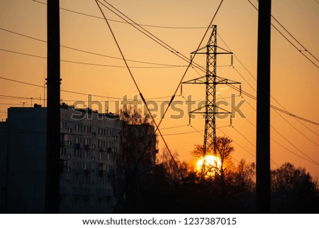 red sunset with sun setting down behind large electricity power line metal poles. dark silhouettes of wires