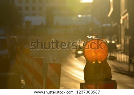 Construction site warning light in direct sunshine with road and more signs in the background