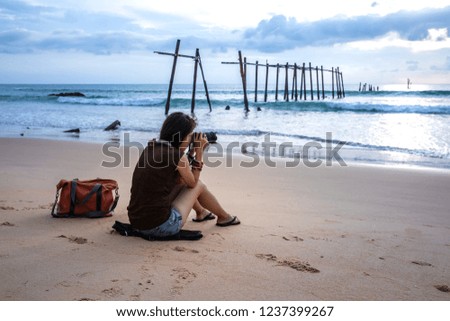 Woman photographer sitting on beach, taking photo at Pilai bridge, the old bridge, Phang Nga, Thailand.
