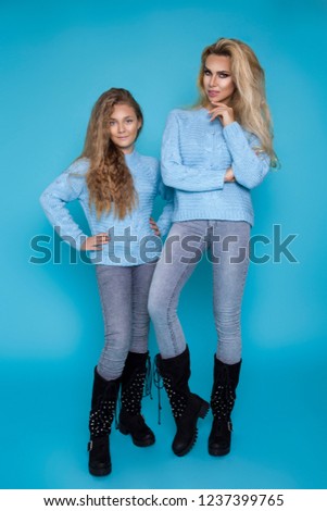 Beautiful blond girls, mother with daughter in autumn winter clothing on a blue background in the studio.