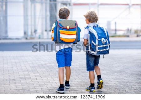 Two little kid boys with backpack or satchel. Schoolkids on the way to school. Healthy adorable children, brothers and best friends outdoors on the street leaving home. Back to school. Happy siblings Royalty-Free Stock Photo #1237411906