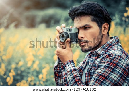 Young hipster man taking photo with old style camera with nature landscape background. Retro and vintage photography concept.