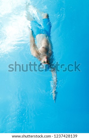 Image on top of young sportsman in blue cap swimming on back in swimming pool