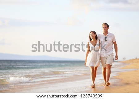 Couple walking on beach. Young happy interracial couple walking on beach smiling holding around each other. Asian woman, Caucasian man. Royalty-Free Stock Photo #123743509