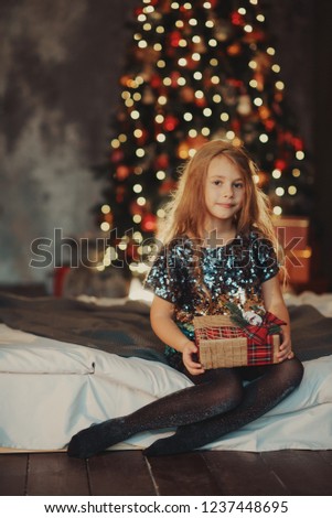 Merry Christmas!happy kid girl with magic gift at home near Christmas tree and fireplace