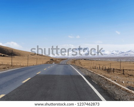 Scenic winter view from the asphalt road in the mountains covered with snow on a background of blue sky and clouds, road to snow mountain and across the meadows.