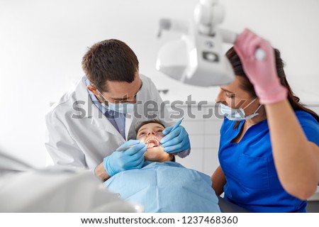 medicine, dentistry and healthcare concept - dentist with mouth mirror and probe checking for kid patient teeth at dental clinic Royalty-Free Stock Photo #1237468360