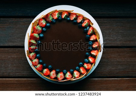 Delicious chocolate cake decorated with fresh strawberries, blueberries, mint, and candied oranges on the brown wooden table. Luxurious dark glaze.  Image for menu or confectionery catalog