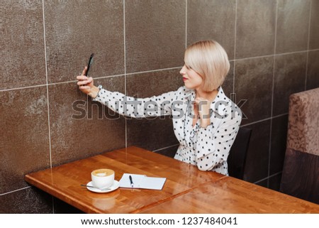 Blonde woman in cafe taking a selfie with mobile phone