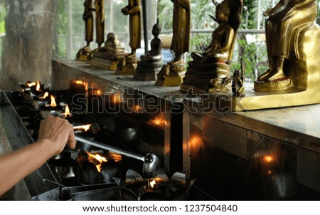 One hand pouring  oil to one of
oil lamps in front of 8 statues of Buddha aligned next to each other. Each of them is for a day of the week.

