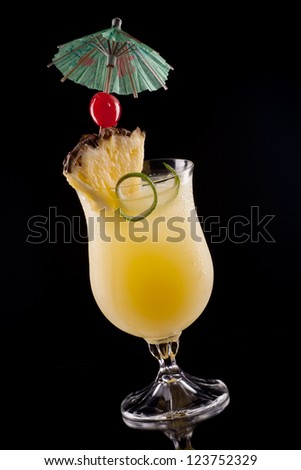 Bahama Mama cocktail over black background on reflection surface, garnished with pineapple flag, maraschino cherry, and lime twist. Most popular cocktails series.