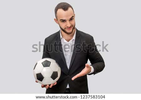 Confident young man in suit stands and hold ball for playing football. He points on it with hand. Isolatede on white background.
